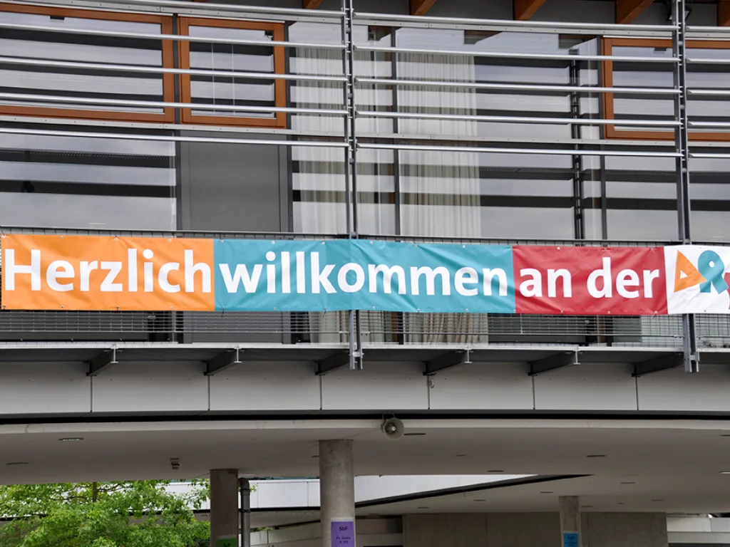Ein Banner mit der Aufschrift „Herzlich willkommen an der“ hängt am Gebäude.
